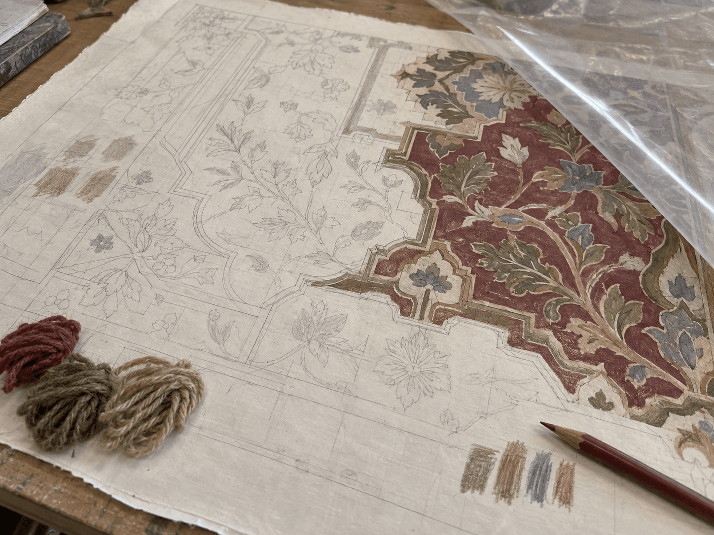 Diseño de alfombra en proceso con trazos de lápiz, zonas de color y muestras de hilo